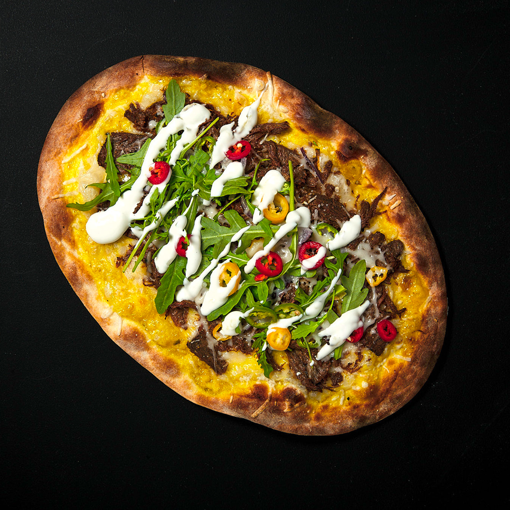Frisch gebackener Crunchy Istanbul Flammkuchen mit knusprigem Boden, orientalisch gewürzten Zutaten, frischen Toppings und aromischer Sauce auf einem Brett serviert.