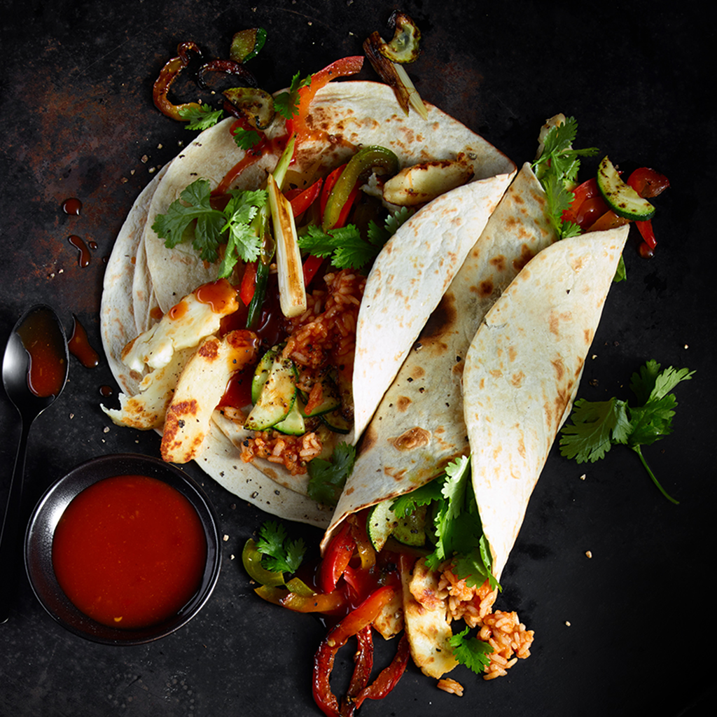 Frisch zubereiteter Halloumi Burrito Fusion gefüllt mit gebratenem Halloumi, knackigem Gemüse und aromatischer Sauce, serviert auf einem Teller.