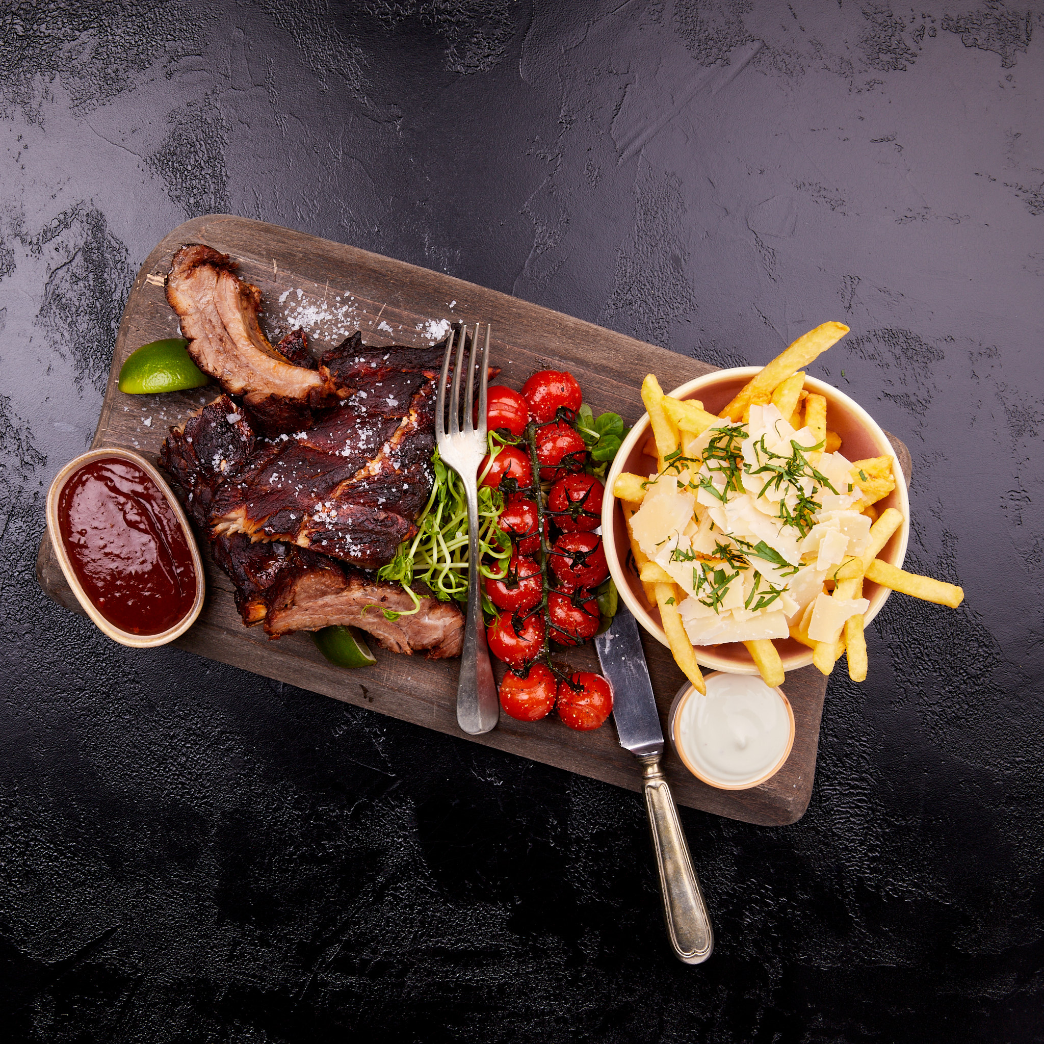 Beef Ribs mit Parmesan Fries, Trüffelmayo, Jalapeño BBQ Dip, Limette, Kirschtomaten und jungen Erbsensprossen.