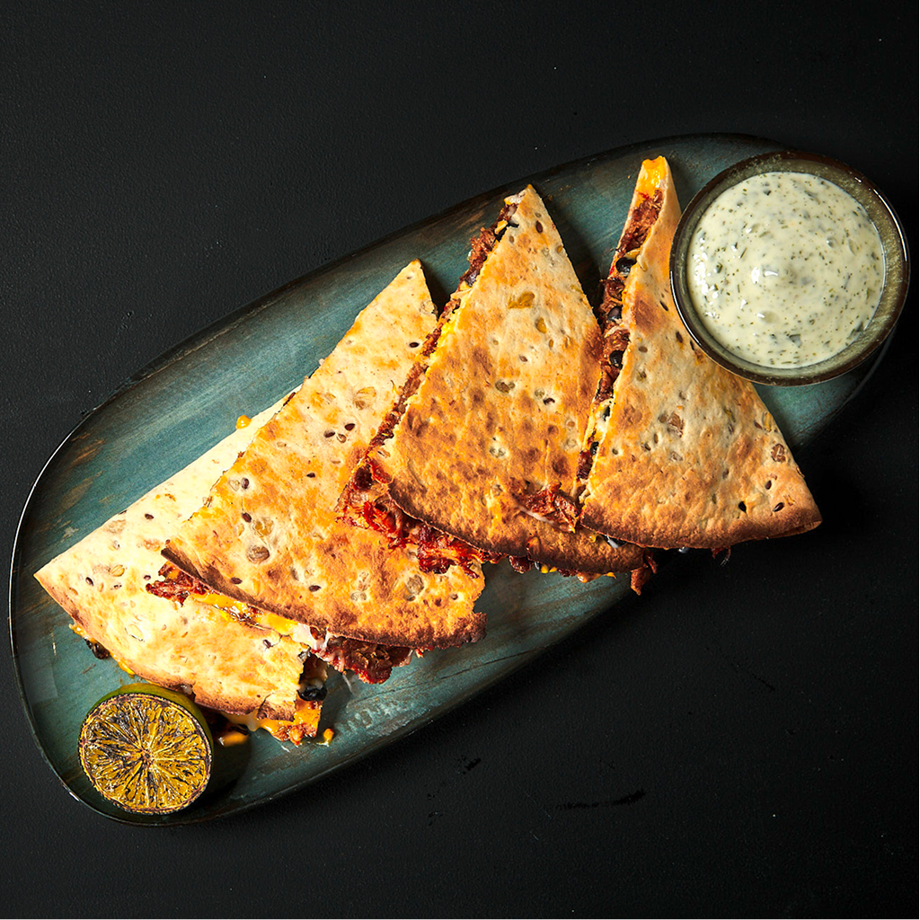 Frisch zubereitete Tex Mex Quesadilla mit knusprig gebratener Tortilla, geschmolzenem Käse, würziger Füllung und frischen Toppings auf einem Teller serviert.